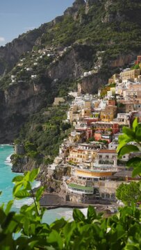 Beautiful Positano village, Amalfi coast, Italy. Camera moves between green leaves, overlooking the beach with turquoise water, colorful houses and mountains in Positano village. Vertical shot
