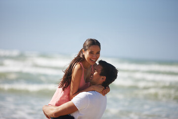Happy couple, hug and beach with embrace for love, care or support on holiday, weekend or outdoor vacation. Man lifting woman with smile for relationship, summer fun or bonding by the ocean coast