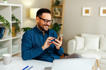 Young smiling man is using a smartphone in home office