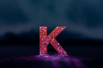 letra K em rosa com brilho em fundo escuro