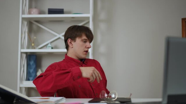 Student preparation for exams. The guy in glasses and a red shirt got upset and jerked off his glasses and threw them on the table, sitting at a table indoors at home