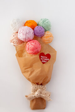 Gift bouquet of multi-colored balls of yarn in craft packaging cotton ribbon and red wooden heart with wish happy mother's day child's lettering on white background