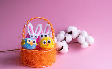 A branch of white cotton, toy eggs with birds in an orange basket and Easter bunnies on a pink...