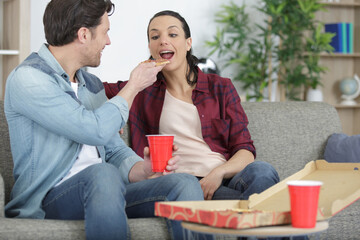 portrait of couple eating pizza on sofa at home