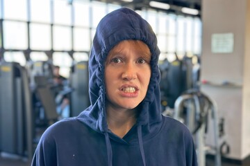 young woman or teenager in a hood feels awkward, stress and sad in the gym