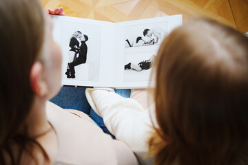 mother and daughter flips through a book with photos of dad and pregnant mom.