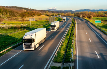 Highway transportation scene with Convoy of white transportation trucks in line on a rural highway...