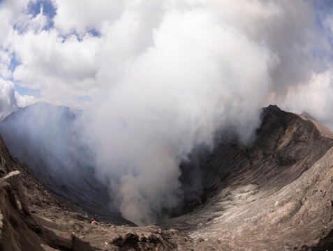 A panoramic view of a vast volcanic crater enveloped in swirling clouds of steam and gas, showcasing nature's dramatic power