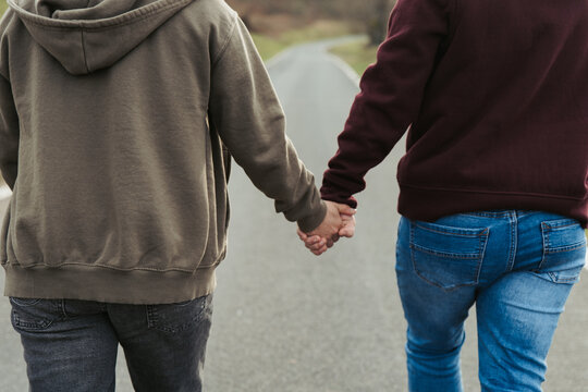 Close-up of anonymous couple holding hands, with a focus on their intertwined fingers, symbolizing love and connection on a quiet walk