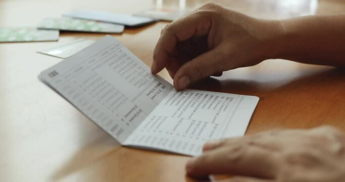 Hands opening bank book to check balance on wooden table
