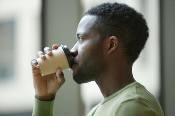 Side view closeup of Black man drinking coffee with paper cup against minimal blurred background
