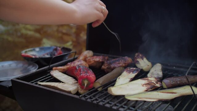 Hand flipping grilled vegetables and meat on a BBQ grill, showcasing a warm, summer outdoor cooking scene