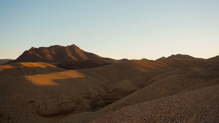 The first light of dawn gently illuminates Timna Valley, highlighting the smooth contours and soft...