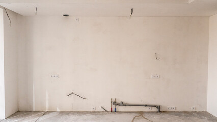 The room is under construction with a rough finish, plastered walls, concrete floor. Wiring of ventilation pipes on a concrete ceiling in a house under construction