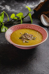 pink ceramic bowl of yellow creamy squash soup with sunflower and pumpkin seeds on top