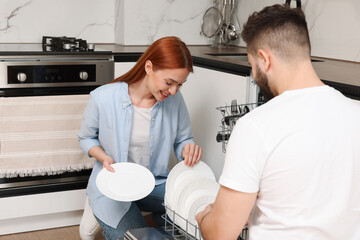 Lovely couple loading dishwasher with plates in kitchen