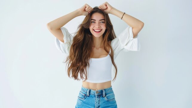 Photo of cheerful beautiful young woman standing isolated on white wall background. Looking at camera showing winning gesture.