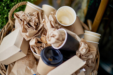 Basket filled with garbage with disposable tableware, top view. Cardboard beverage cups with plastic lids, fast food packaging, used napkins, copy space