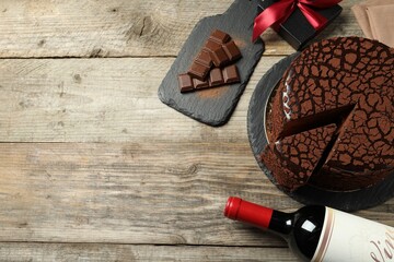 Delicious truffle cake, bottle of wine, chocolate pieces and gift box on wooden table, flat lay....