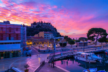 A colorful sky at dawn above the Château de Cassis hilltop fortified castle and the shops and...