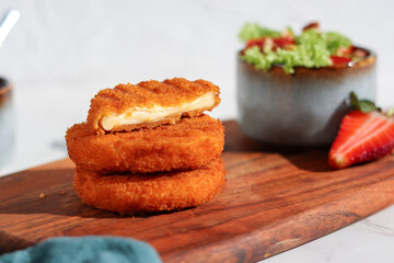 Fresh made and cutted fried camembert cheese with a side of fresh salad on wooden plate, white marble table