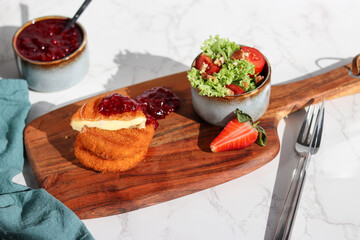 A portion of fresh made fried camembert cheese with cranberry sauce on top and a side of fresh salad on wooden plate