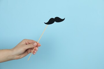 Woman with fake paper mustache on light blue background, closeup. Space for text