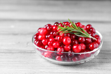 Fresh ripe cranberries and rosemary in bowl on grey wooden table, closeup