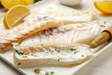 Fresh raw cod fillets with spices, lemon and brush on white wooden table, closeup