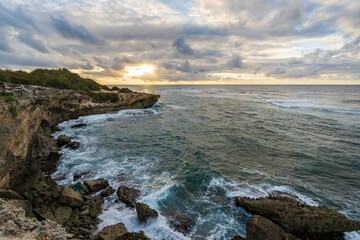 The sun slowly rises over jagged cliffs, which meet the rough turquoise waters of the Pacific Ocean...