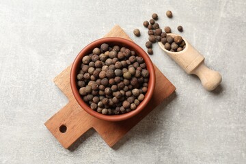 Aromatic allspice pepper grains in bowl and scoop on grey table, top view