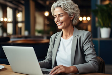 Confident mature businesswoman in her 50s with stylish silver hair working on her laptop at a...