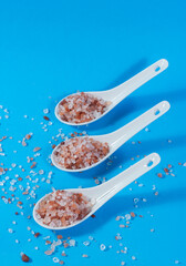 Composition of ceramic teaspoons with Himalayan pink salt on blue background.