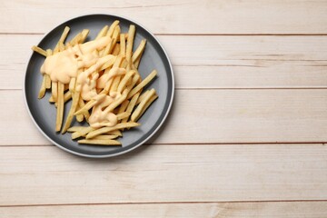 Delicious french fries with cheese sauce on wooden table, top view. Space for text
