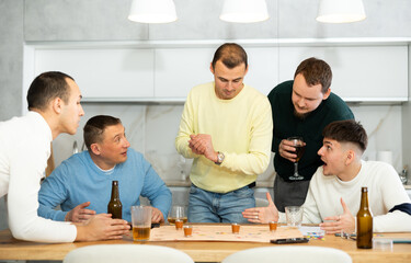 Group of adult friends excitedly playing board games and drinking beer at home