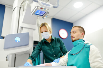 Female radiologist going to made x-ray shot of young man hand in x-ray room in modern clinic. Patient wearing in protect lead apron