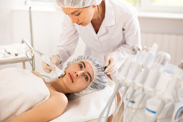 Young female patient receiving facial procedure with high frequency ultrasonic vibration attachment to enhance efficacy of skincare products and improving skin texture. Modern hardware cosmetology