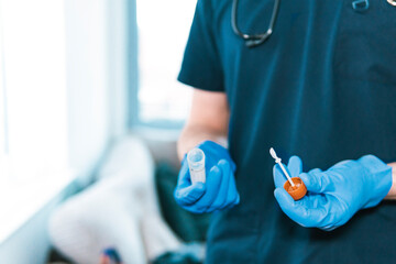 Close-up of anonymous medical practitioner's hands, gloved in blue, holding a sterile specimen container and applicator