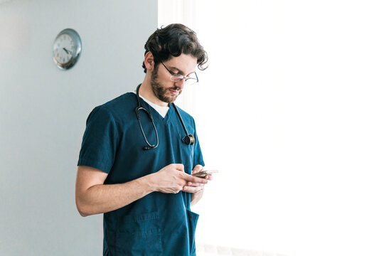 A focused male healthcare worker in scrubs checks his smartphone, possibly reviewing patient information or coordinating care