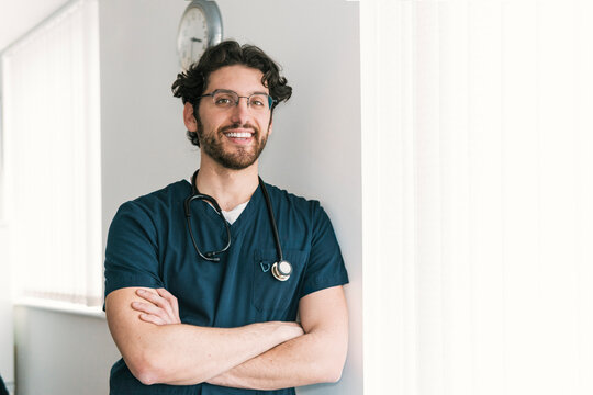 A pensive male healthcare worker with arms crossed stands by a clock, symbolizing timely medical services