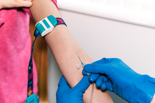 The image captures a moment during a blood sampling procedure where anonymous professional in blue gloves expertly inserts a butterfly needle into a patient's vein