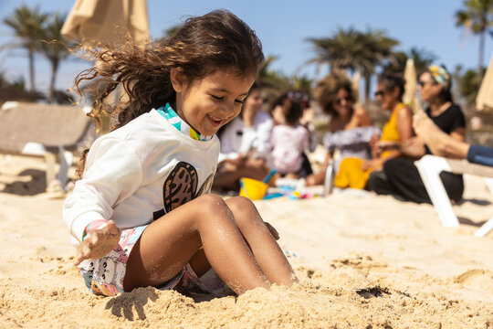 Joyful child playing in sand with family at the beach