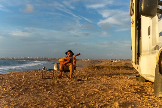 Nomadic musician composes by the sea at sunset