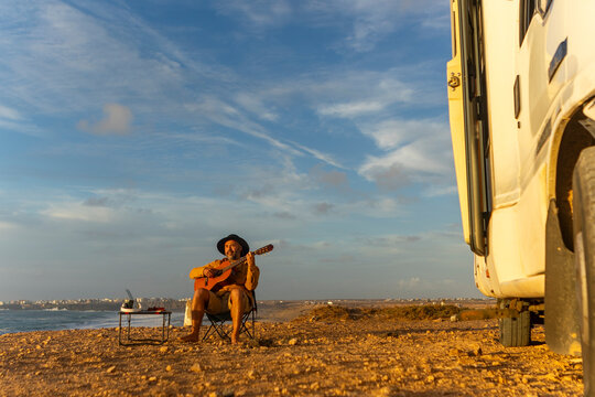 Nomadic Musician Composing by the Sea at Sunset