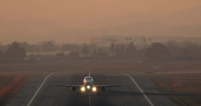 Airplane with headlights and wingtip lights takes off from runway at twilight