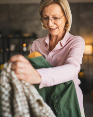 One mature blonde woman at home choose and sort clothes on hanger