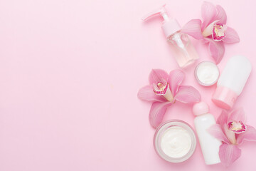 Bottles and jars with cream and orchids on color background, top view - obrazy, fototapety, plakaty