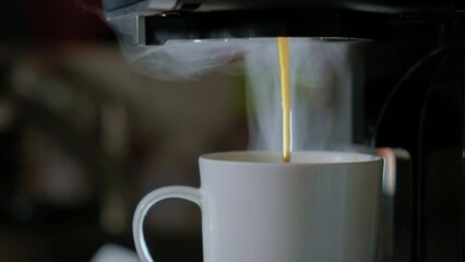 Close up view of hot black coffee pouring from the machine to white cup. Fresh cafe in the kitchen of home or office. 