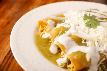 Green enchiladas. Typical Mexican dish made with a folded or rolled corn tortilla filled with shredded chicken and covered with spicy green sauce, cream, grated cheese and onion. - 775442307