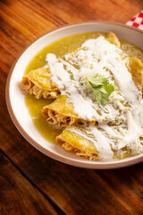 Green enchiladas. Typical Mexican dish made with a folded or rolled corn tortilla filled with shredded chicken and covered with spicy green sauce, cream, grated cheese and onion. - 775442728
